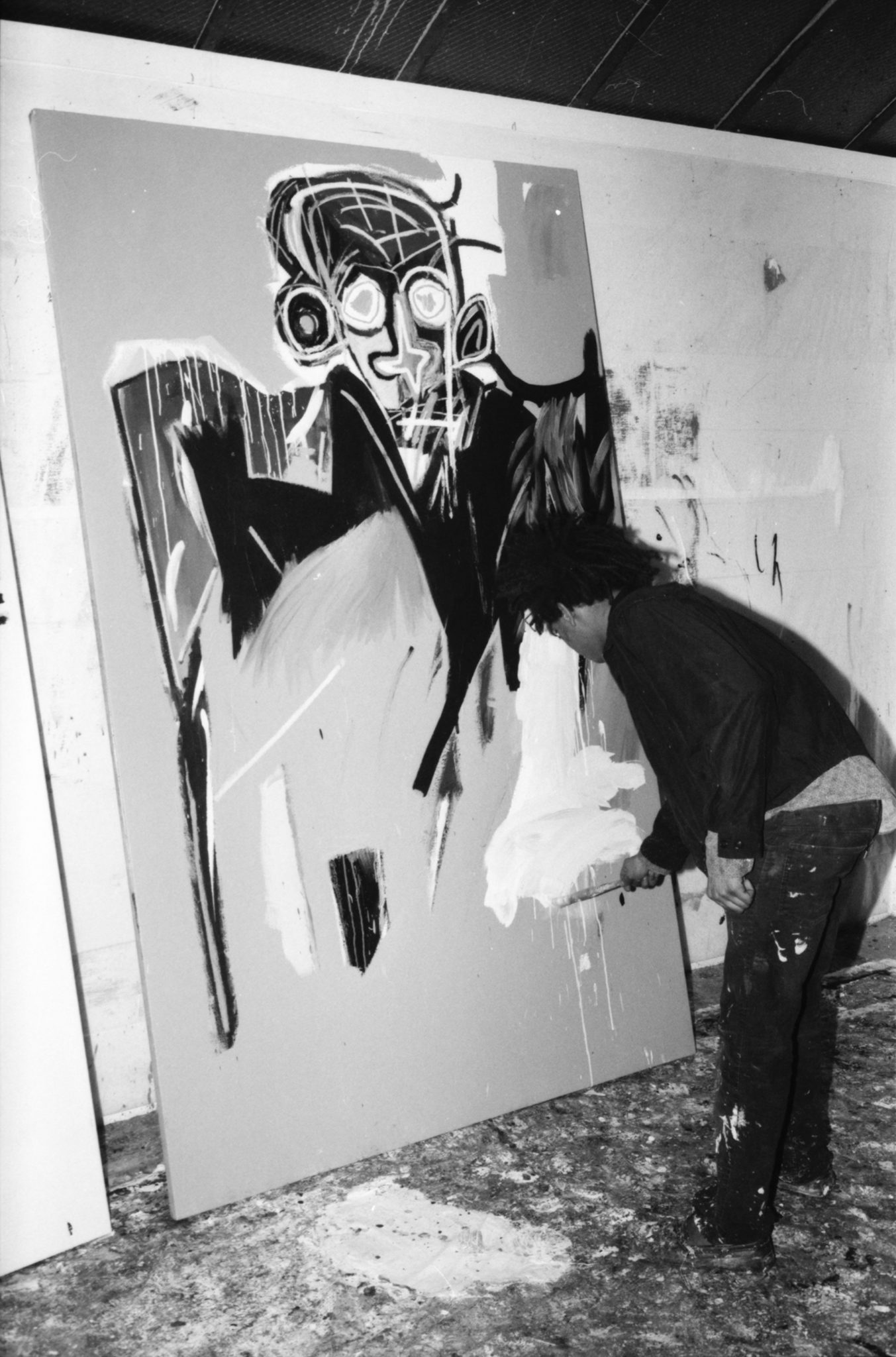 Black and white photograph of Jean-Michel Basquiat painting in his studio